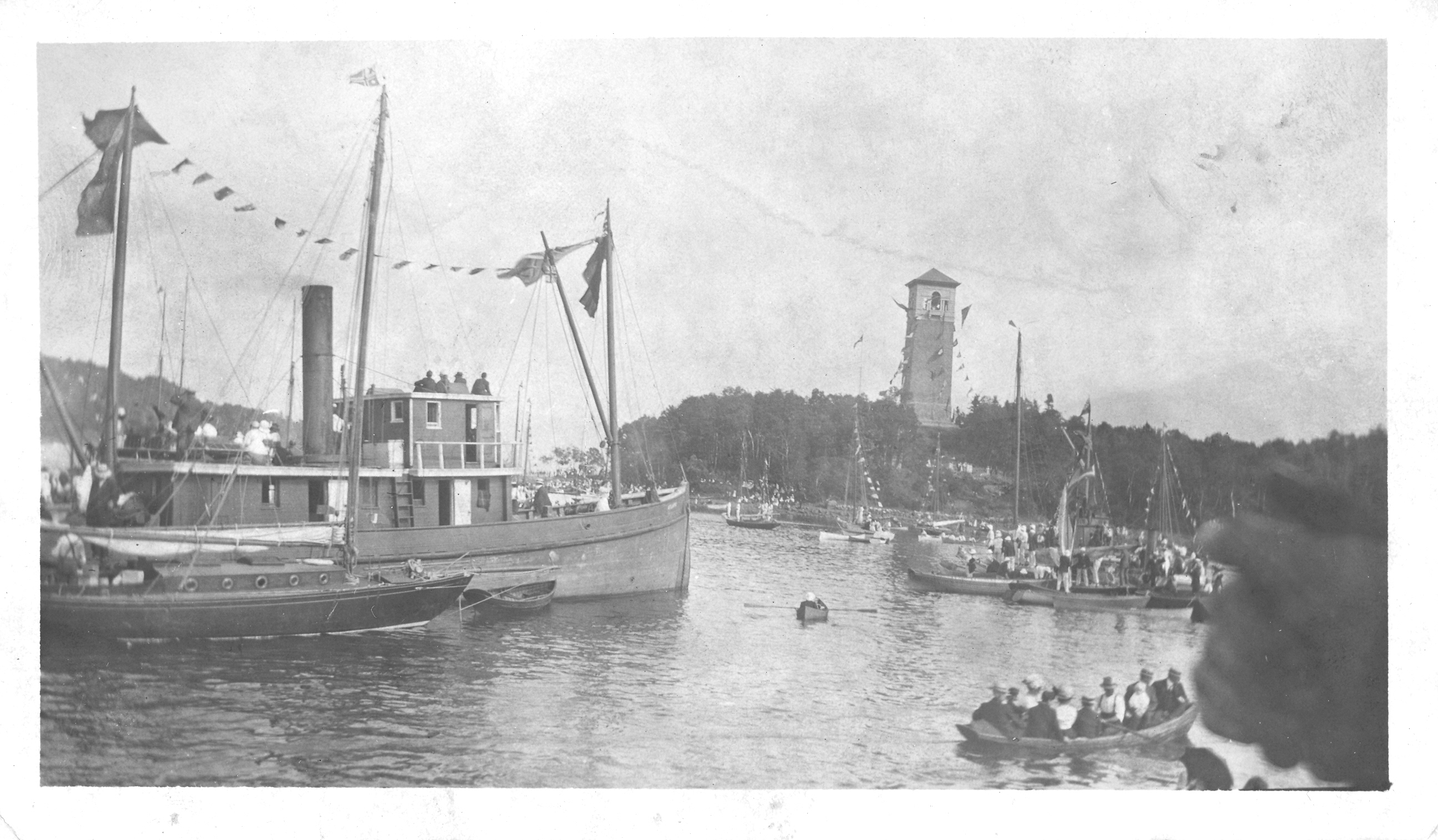 White photo of ships and boats in the harbour with the Dingle Tower in the background