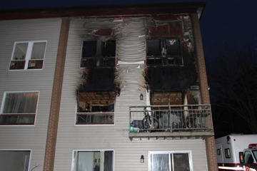Image of a three storey building with blackened and melted vinyl on the upper two units from a recent structure fire.