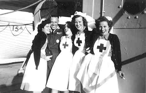 Black & white photo of 4 young women in Red Cross uniforms and 1 male soldier on the deck of a ship.