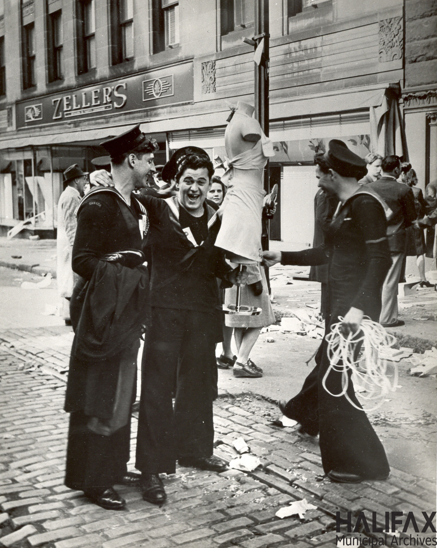 Black and white photograph of celebrating sailors holding a mannequin outside a Zeller's store