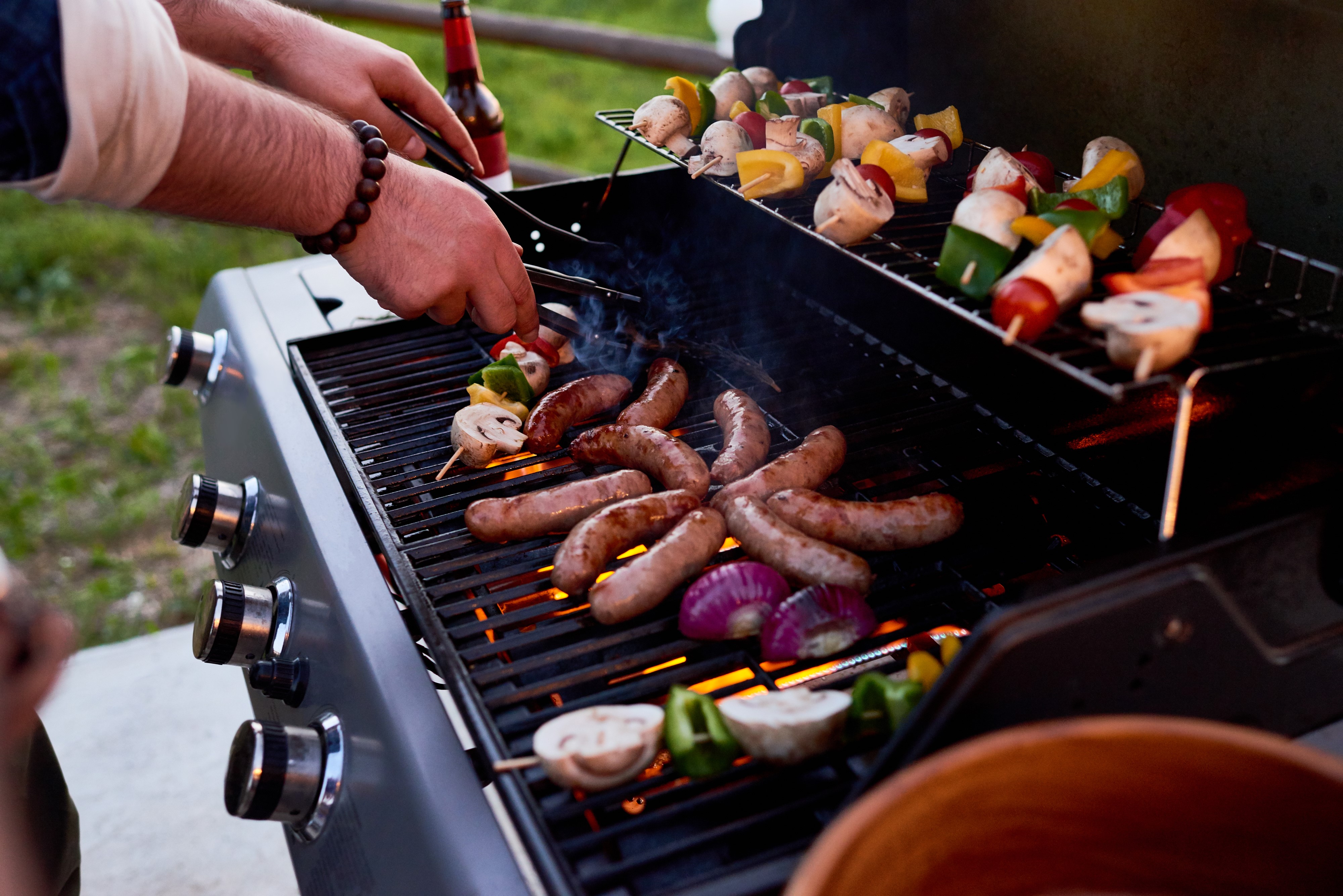 a close up on a person barbecuing meat and vegetables on a propane bbq