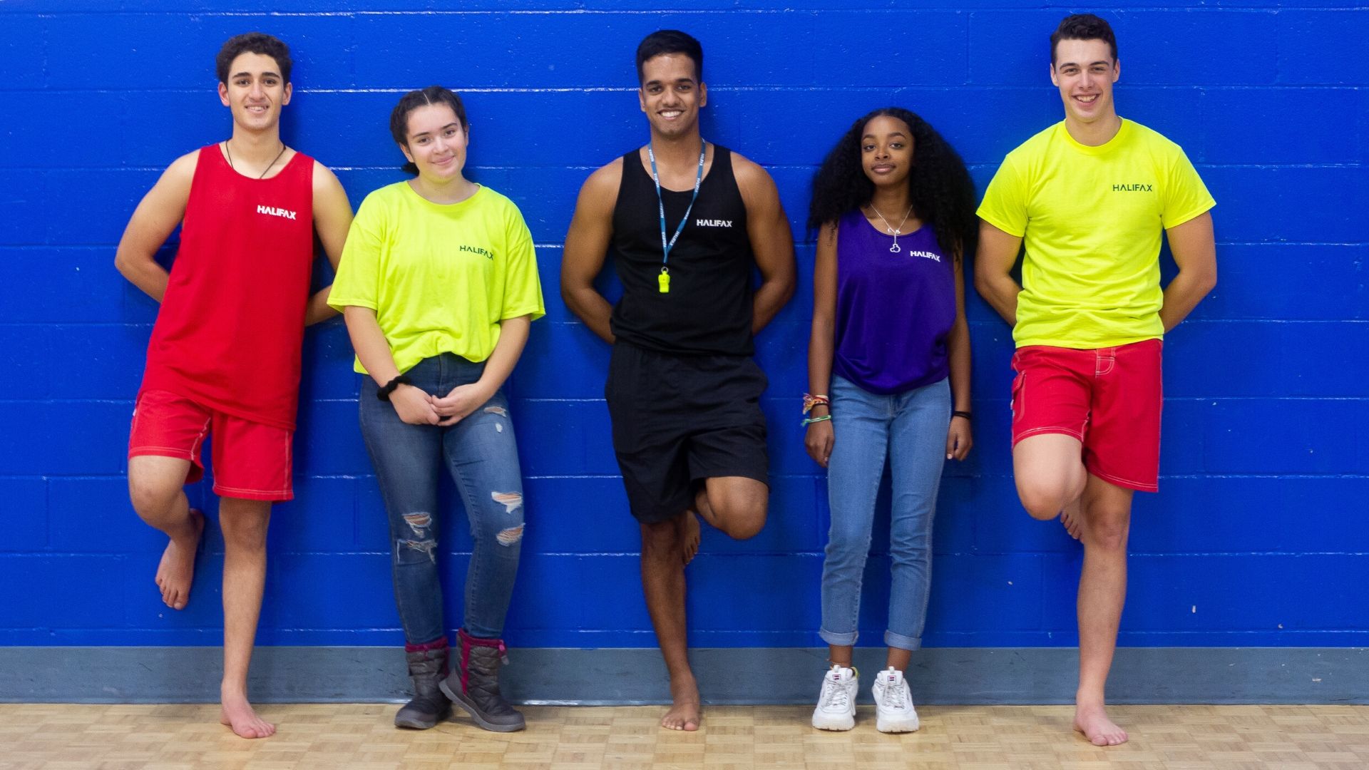 A diverse group of youth recreation employees standing in front of a blue wall at a municipal pool.