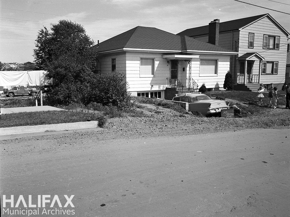 Black and white photograph of a house with no curb in front of it.
