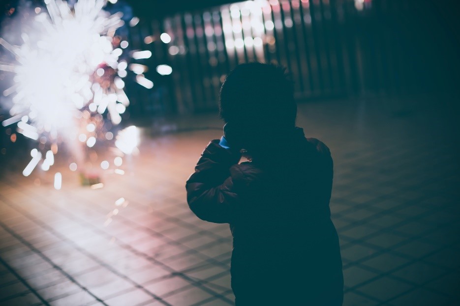 Child holding hands up to it's ears behind loud fireworks.