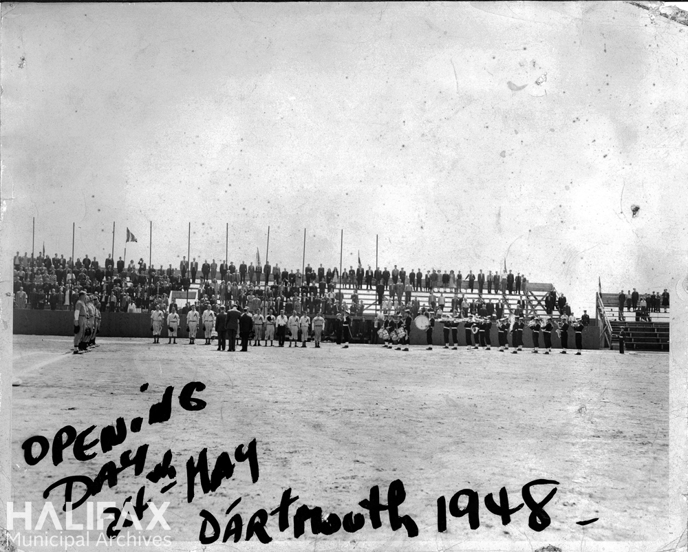 Black and white photograph of baseball teams lined up for opening day ceremony with crowd in background