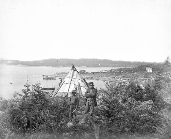 A man and a child stand in tall grass on Turtle Grove, a settlement on the Dartmouth side of the harbour, now known as Tufts Cove. 
