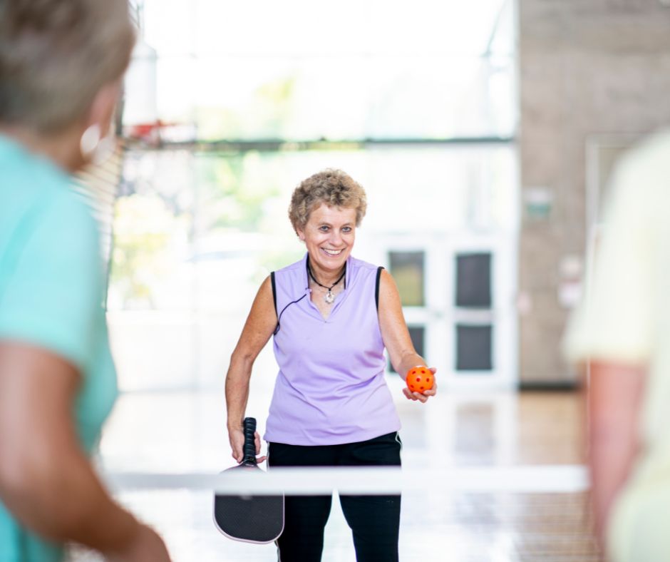 three seniors playing pickleball indoors