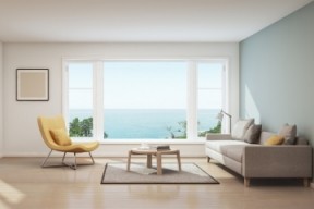 The interior of a modern, minimalist living room. The ocean is visible outside the window.
