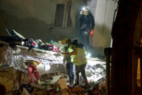 a dark image of people dressed in safety gear with flashlights searching through a damaged property
