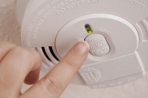 Close up image of a finger pushing the test button on a smoke alarm