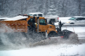 A side view of a large snow plow clearing a wide street of snow in winter.