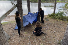 People are setting up a tarp shelter in the woods