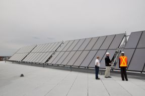 three employees stand next to very large solar panels on the top of a building